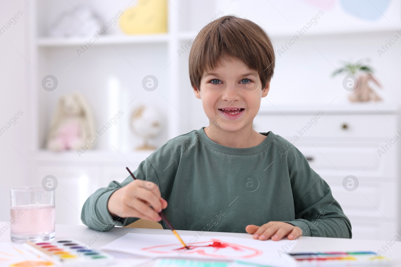 Photo of Happy boy drawing at white table in kindergarten