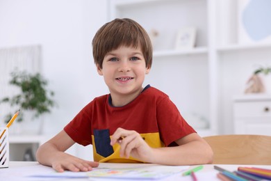 Photo of Happy boy drawing at white table in kindergarten