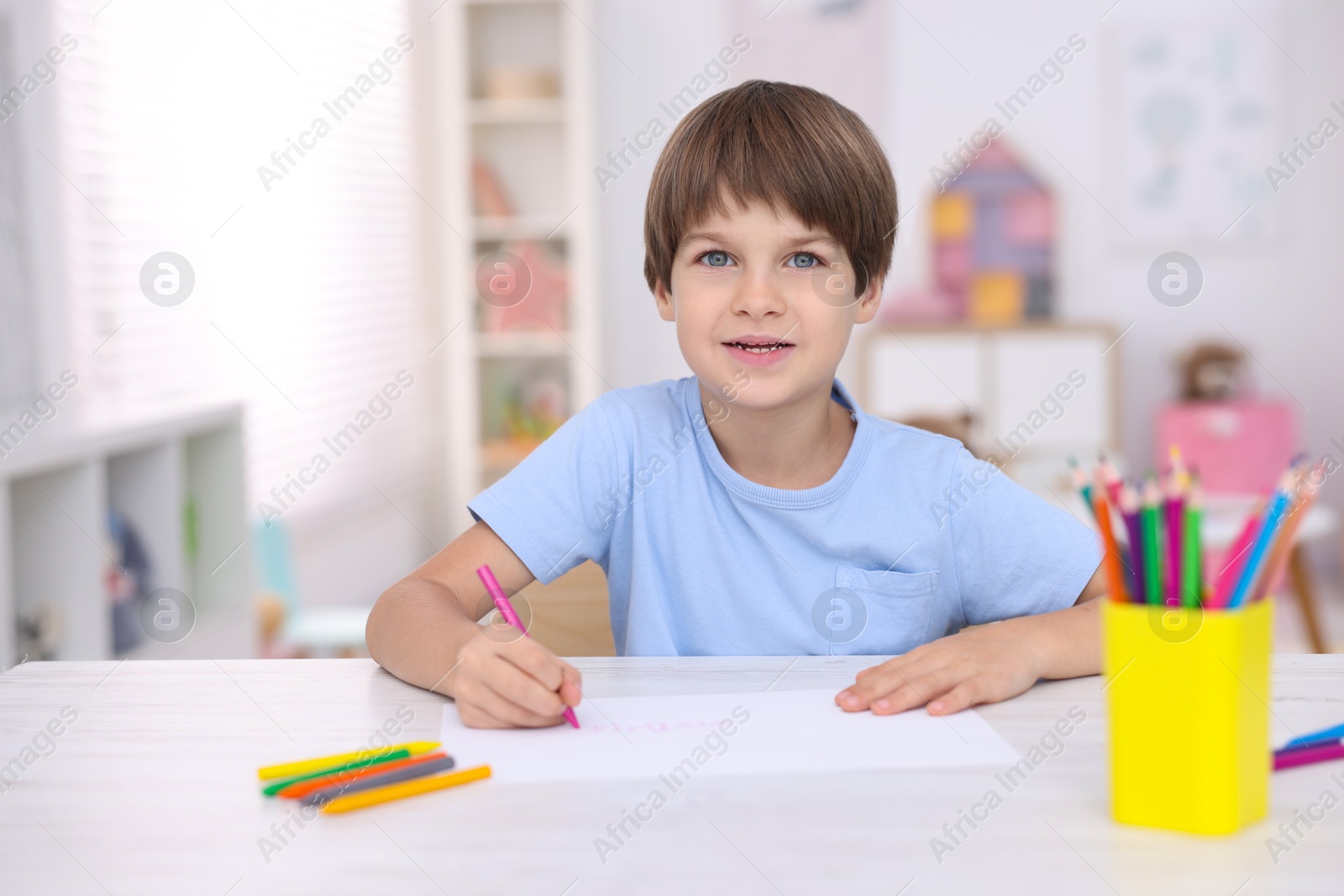 Photo of Cute boy drawing at white table in kindergarten