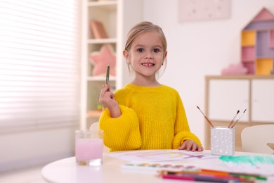 Photo of Smiling girl drawing at white table in kindergarten