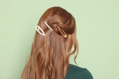 Photo of Teenage girl with stylish hair clips on light green background, back view