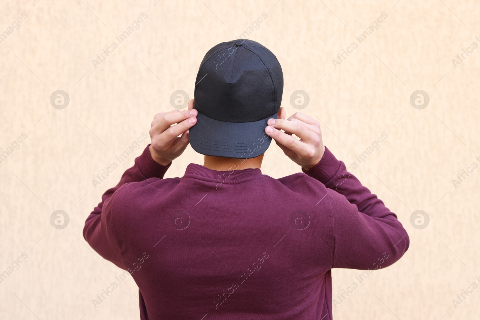 Photo of Man in stylish baseball cap near beige wall, back view. Mockup for design