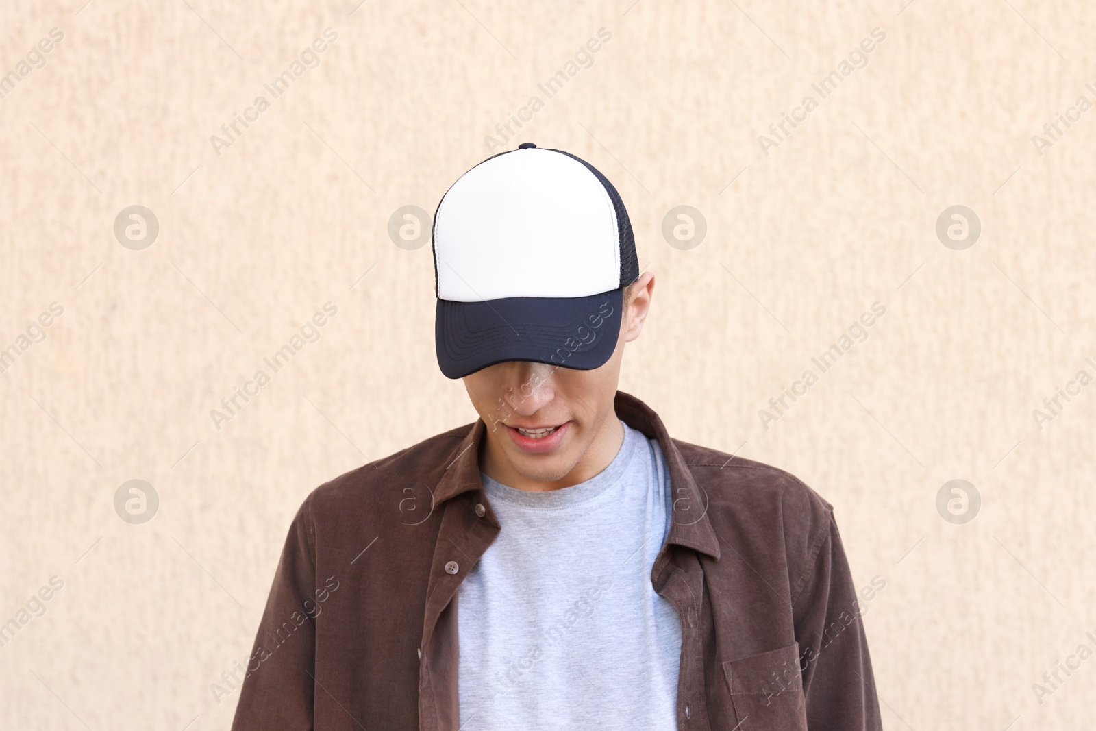 Photo of Smiling man in stylish baseball cap near beige wall. Mockup for design