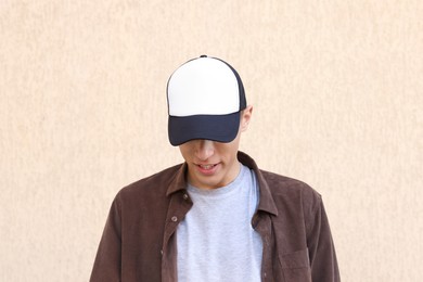 Photo of Smiling man in stylish baseball cap near beige wall. Mockup for design