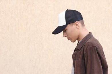 Photo of Man in stylish baseball cap near beige wall. Mockup for design