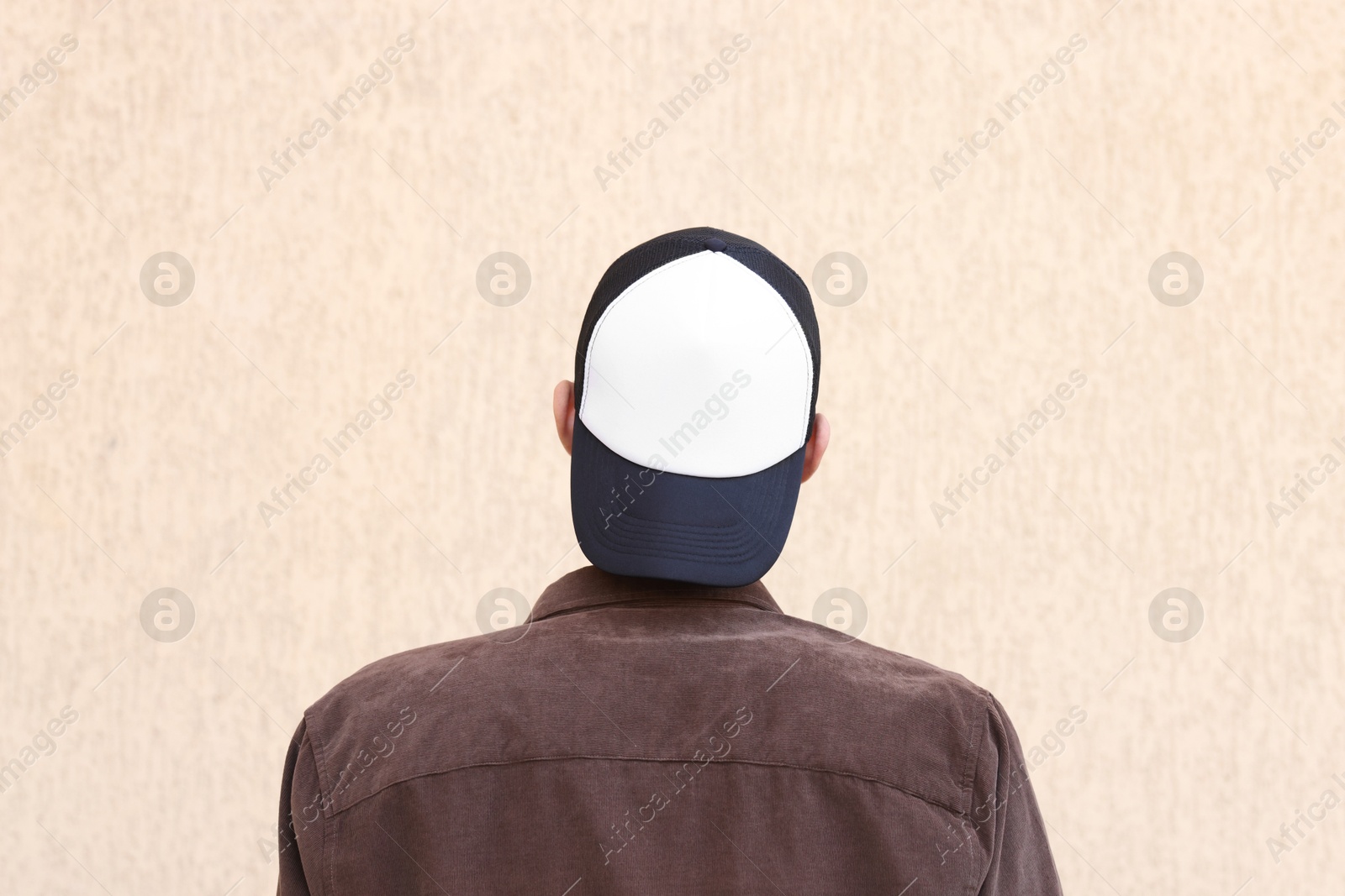 Photo of Man in stylish baseball cap near beige wall, back view. Mockup for design