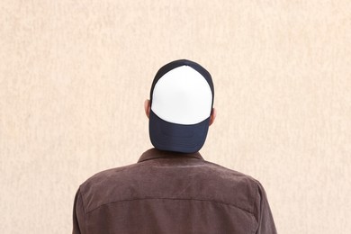 Photo of Man in stylish baseball cap near beige wall, back view. Mockup for design