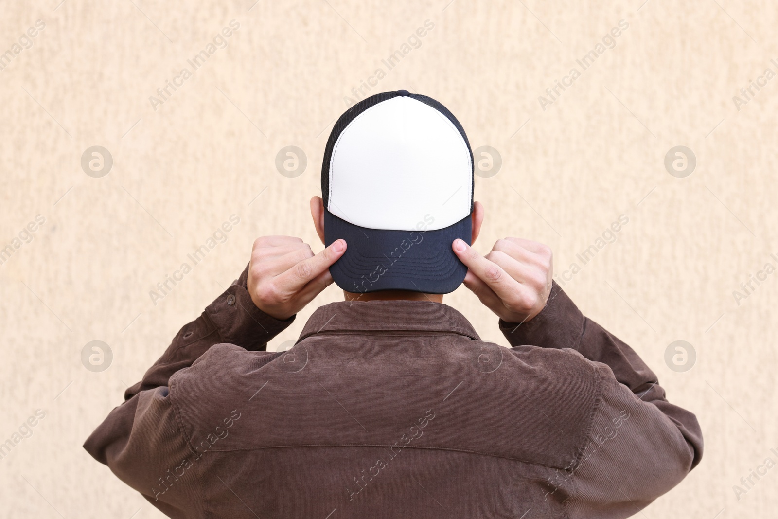 Photo of Man in stylish baseball cap near beige wall, back view. Mockup for design