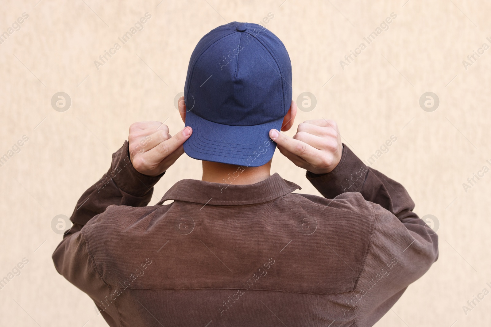 Photo of Man in stylish baseball cap near beige wall, back view. Mockup for design