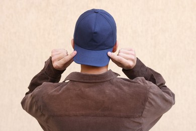 Photo of Man in stylish baseball cap near beige wall, back view. Mockup for design