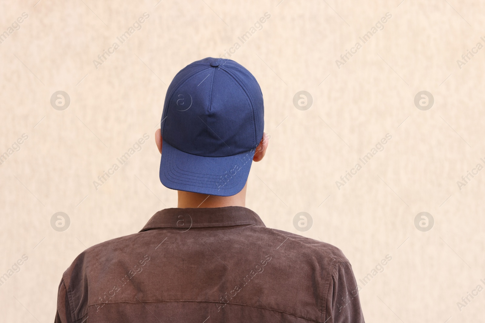 Photo of Man in stylish baseball cap near beige wall, back view. Mockup for design