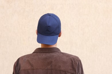 Photo of Man in stylish baseball cap near beige wall, back view. Mockup for design