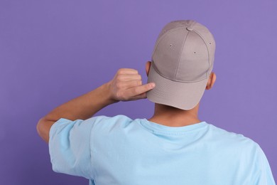 Photo of Man in stylish baseball cap on violet background, back view. Mockup for design