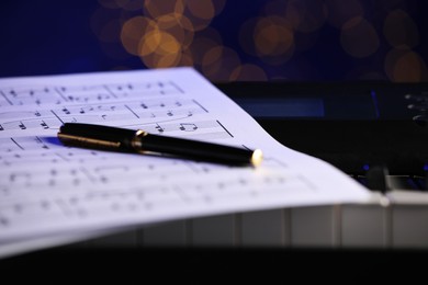 Sheet with musical notes and pen on piano against blurred lights, closeup. Bokeh effect