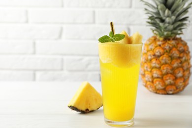 Photo of Tasty pineapple cocktail with mint in glass on light table against white brick wall, space for text