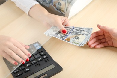 Photo of Cashier giving dollar banknotes to client at table in money exchange, closeup