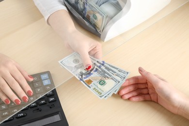 Photo of Cashier giving dollar banknotes to client at table in money exchange, closeup