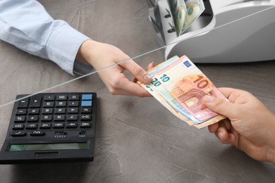 Photo of Client giving euro banknotes to cashier at table in money exchange, closeup