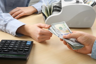 Photo of Client giving dollar banknotes to cashier at table in money exchange, closeup