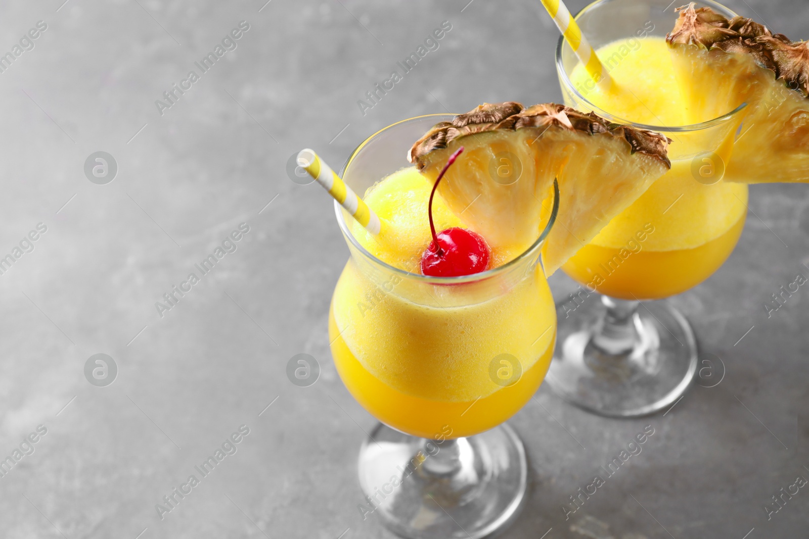 Photo of Tasty pineapple cocktail in glasses served on grey table, closeup. Space for text