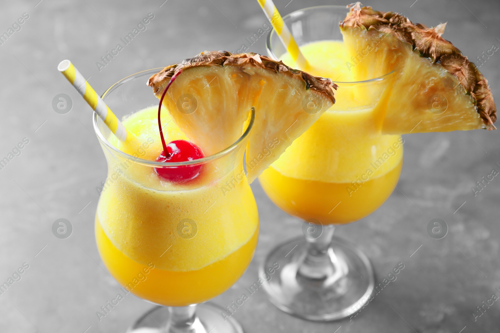 Photo of Tasty pineapple cocktail in glasses served on grey table, closeup