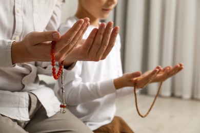 Photo of Muslim man and his son with beads praying indoors, closeup