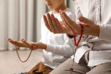 Photo of Muslim man and his son with beads praying indoors, closeup