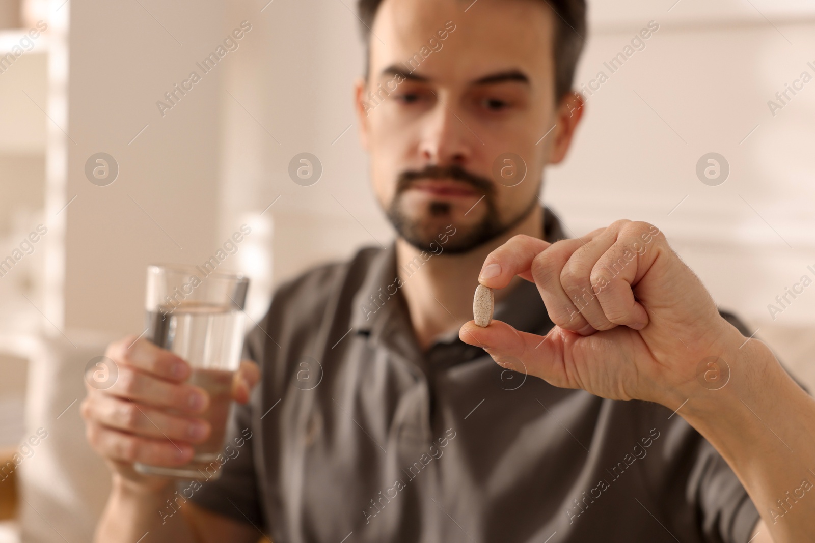 Photo of Man with pill and glass of water at home, selective focus