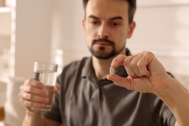 Photo of Man with pill and glass of water at home, selective focus