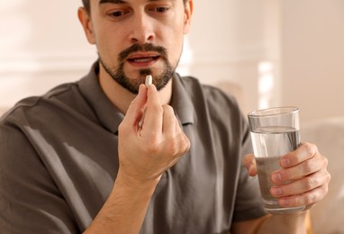 Photo of Man with glass of water taking pill at home, closeup