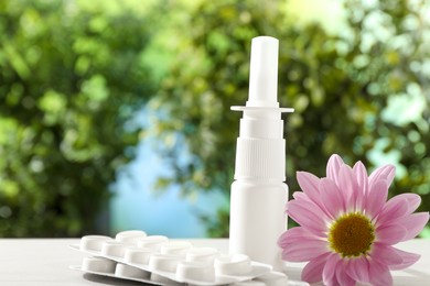 Photo of Allergy treatment. Nasal spray, pills and flower on white table against blurred background. Space for text