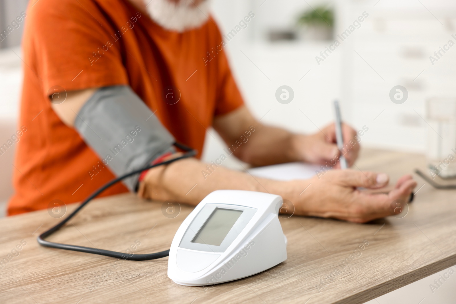 Photo of Senior man writing results of blood pressure measurement at table indoors, selective focus