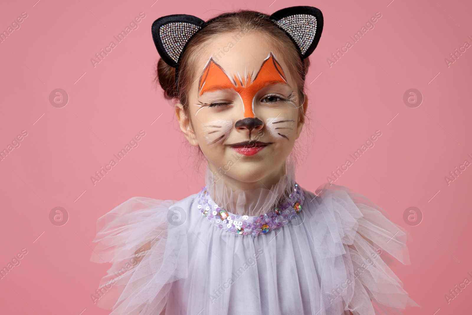 Photo of Cute girl with painted face and ears as cat on pink background