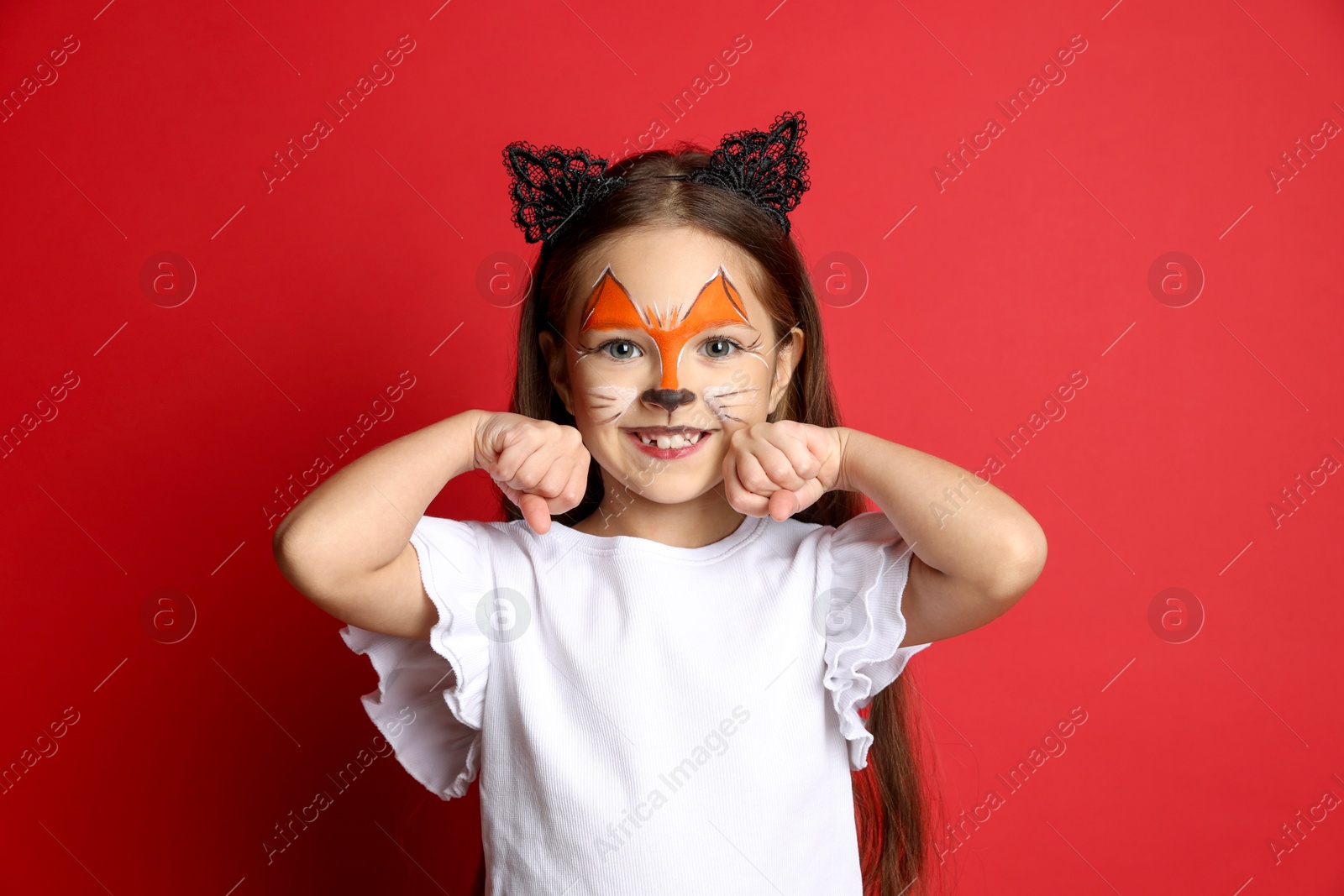 Photo of Cute girl with painted face and ears as cat on red background