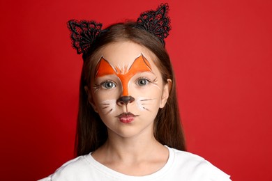 Photo of Cute girl with painted face and ears as cat on red background