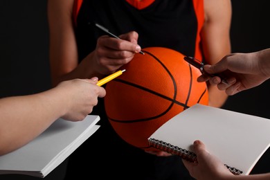 Photo of Sportsman signing autograph on basketball ball against black background, closeup