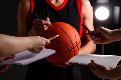 Photo of Sportsman signing autograph on basketball ball against dark background, closeup