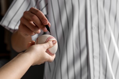 Photo of Sportsman signing autograph on baseball ball against black background, closeup