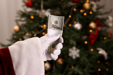 Photo of Santa Claus with dollar banknotes near Christmas tree indoors, closeup. Space for text