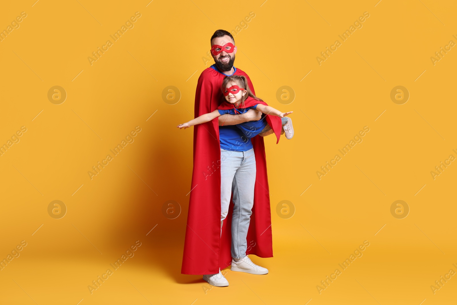 Photo of Father and his cute little daughter wearing superhero costumes on orange background