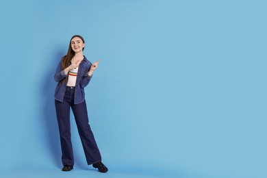 Photo of Smiling woman in stylish jeans pointing at something on light blue background. Space for text