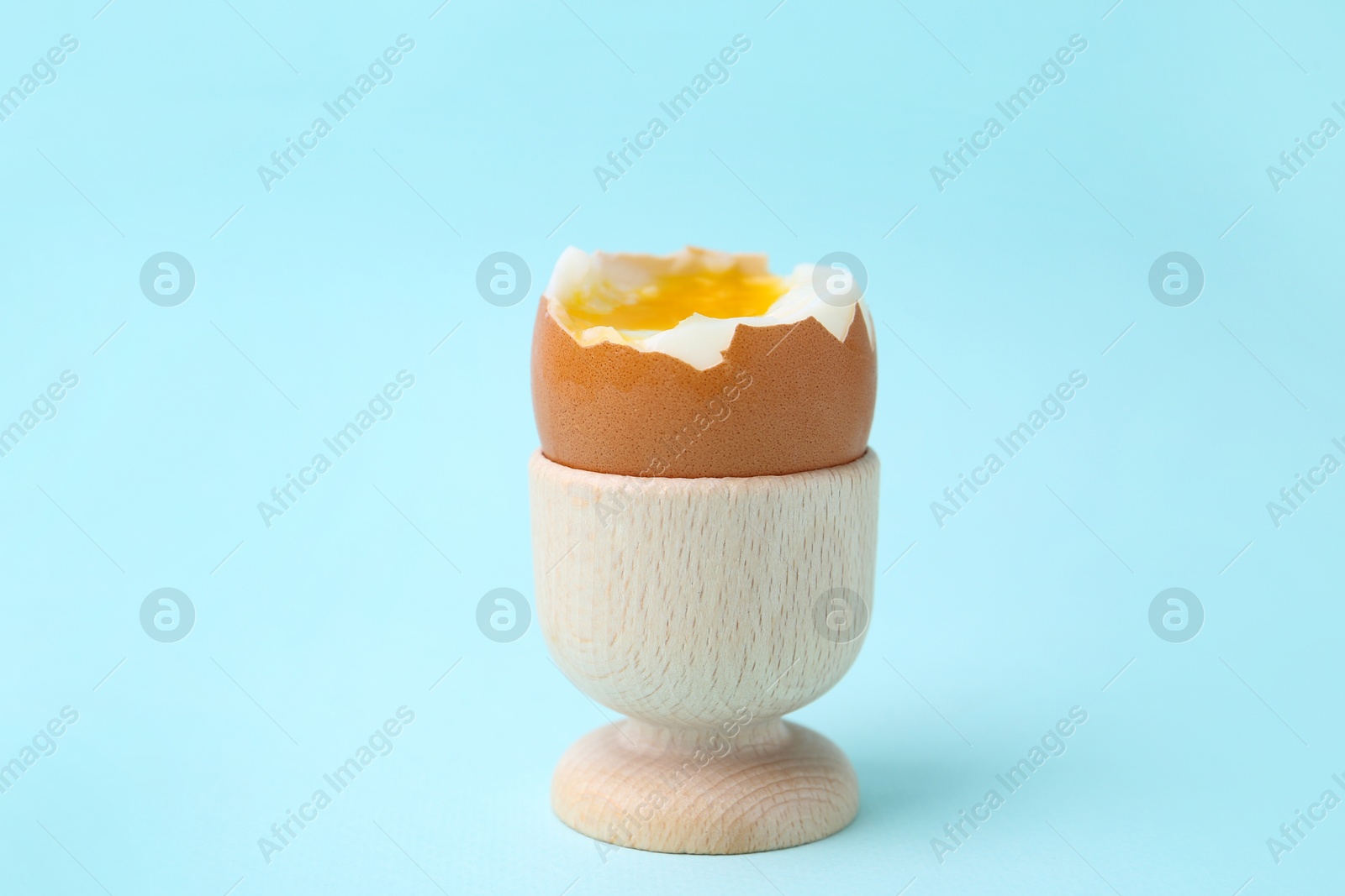 Photo of Soft boiled egg in eggcup on light blue background, closeup