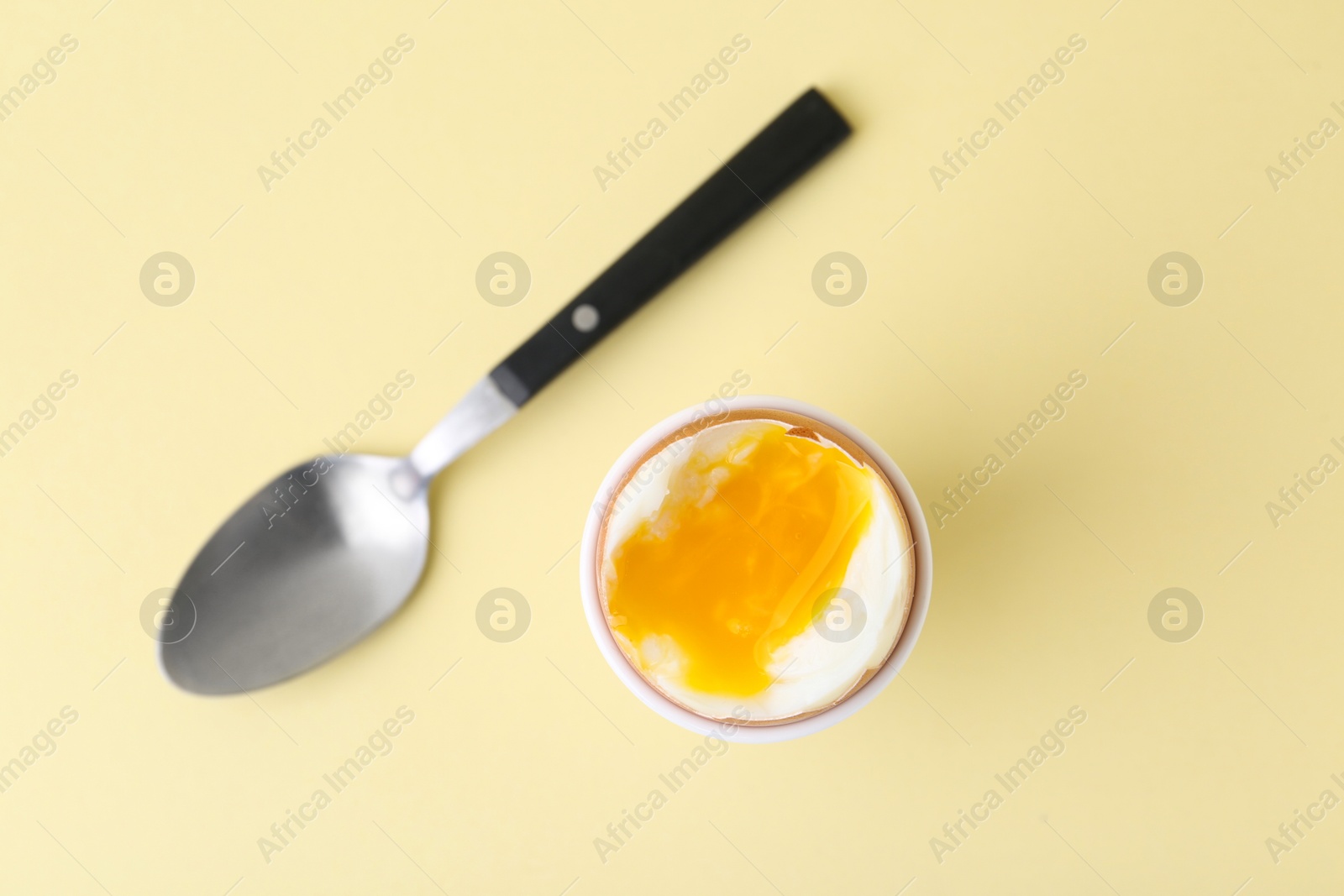 Photo of Soft boiled egg in eggcup and spoon on beige background, top view