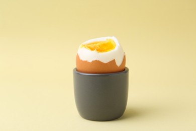 Photo of Soft boiled egg in eggcup on beige background, closeup