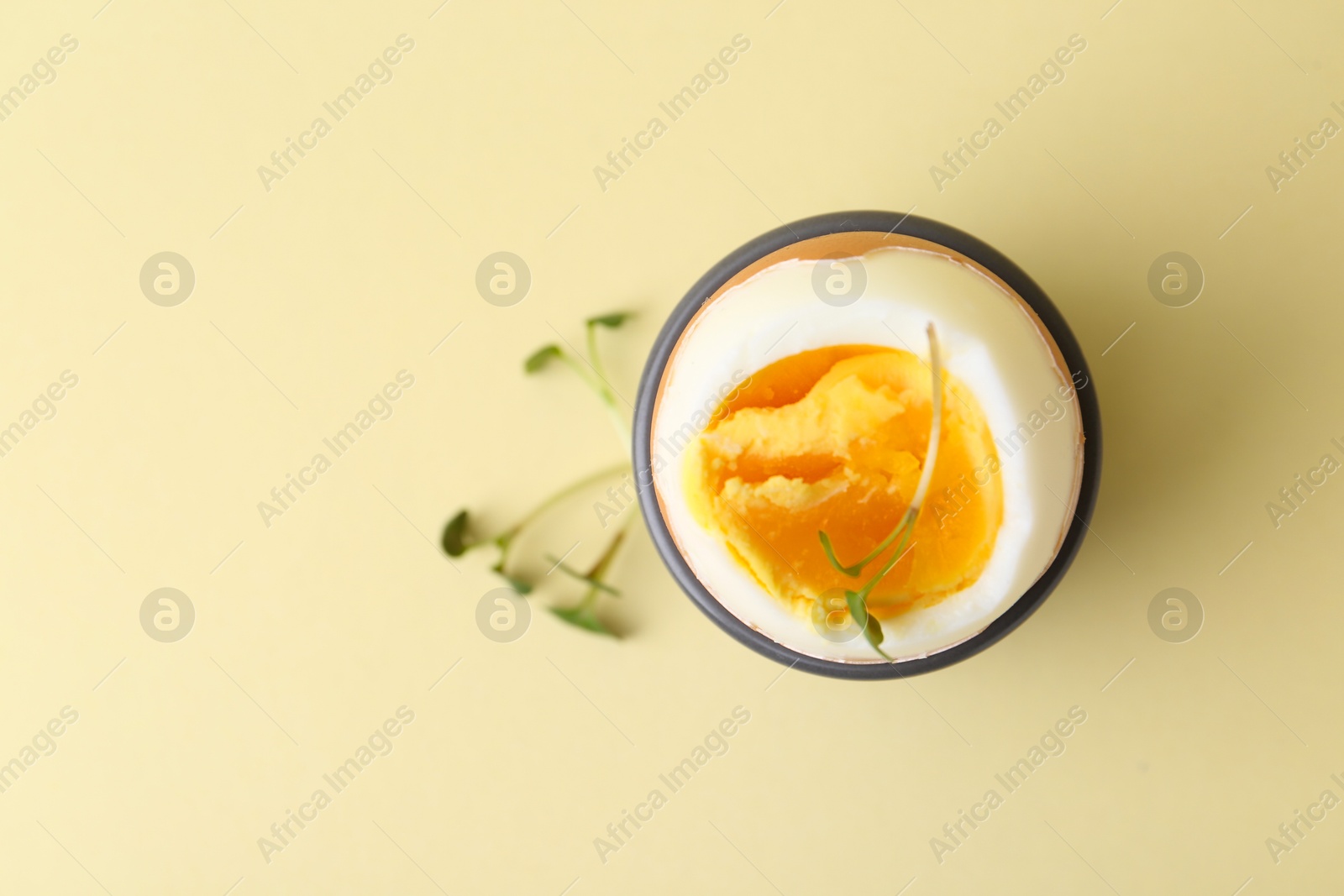 Photo of Soft boiled egg in eggcup on beige background, top view