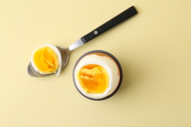 Photo of Soft boiled egg in eggcup and spoon on beige background, top view