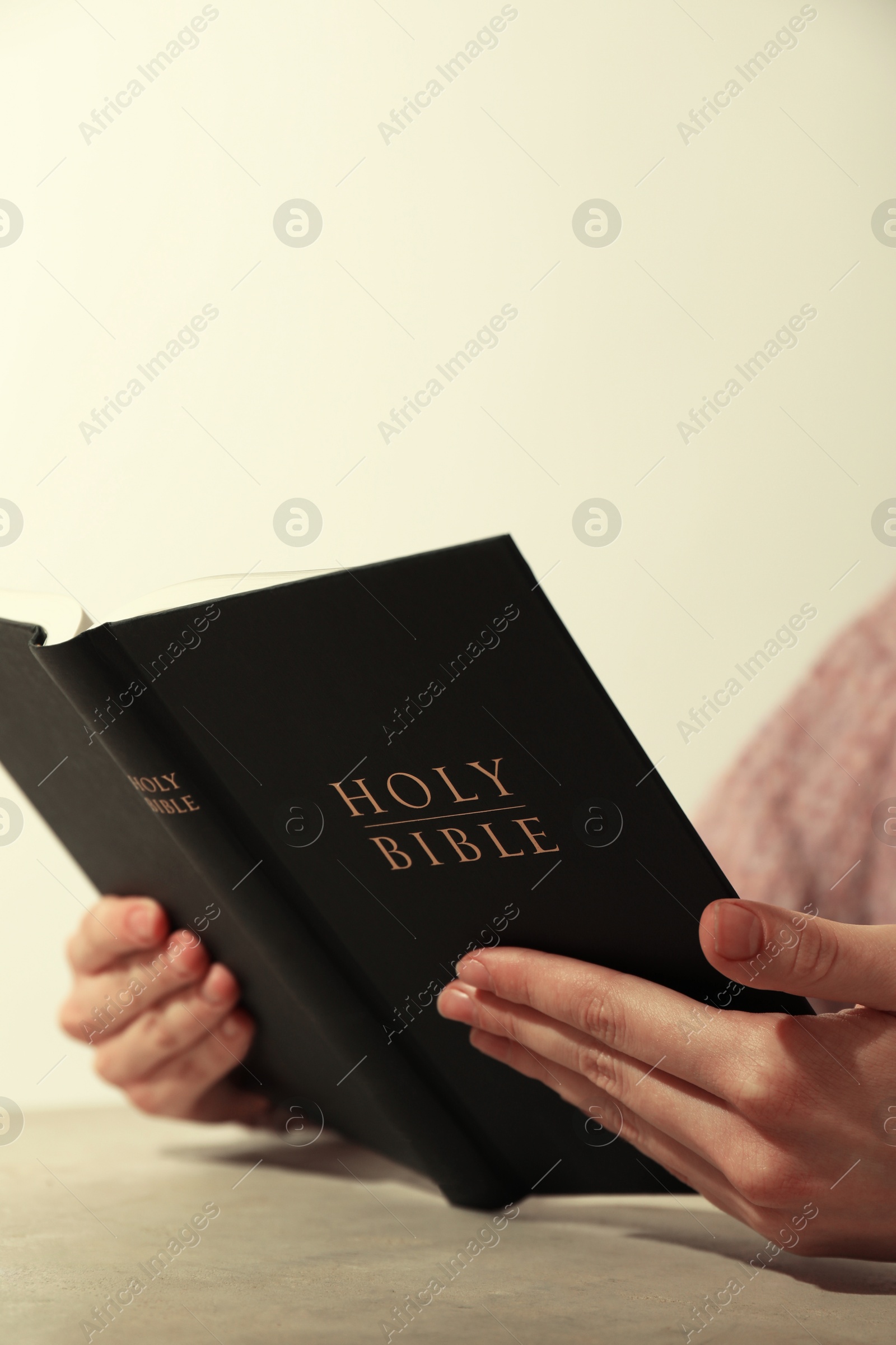 Photo of Woman reading Holy Bible at beige table, closeup