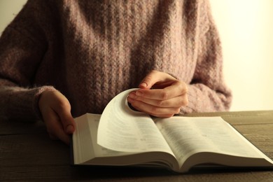 Photo of Woman reading Holy Bible at wooden table, closeup