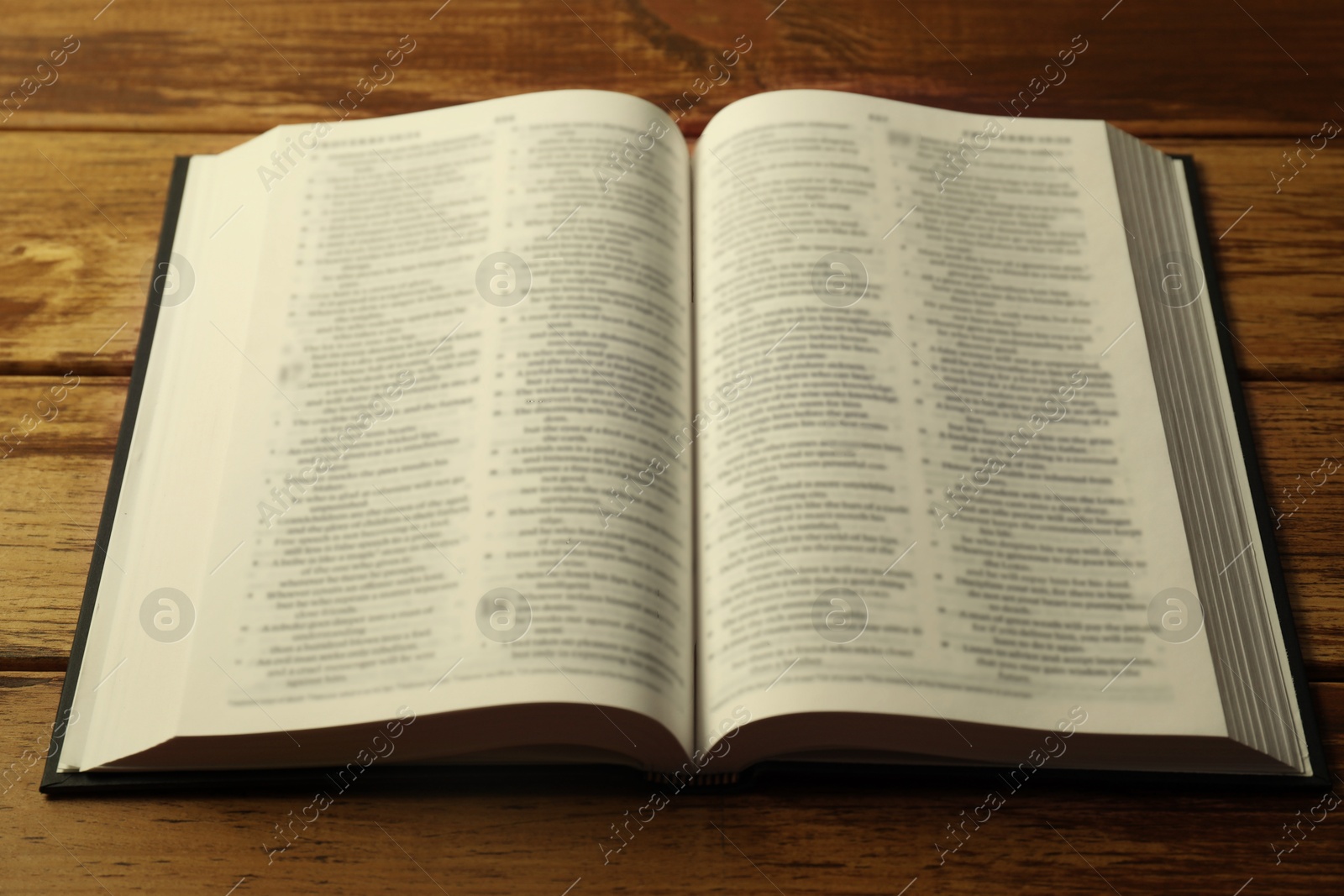 Photo of Open Holy Bible in English language on wooden table, closeup