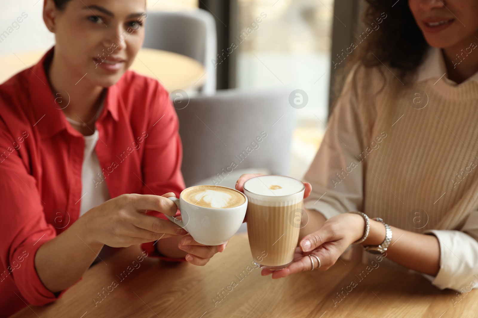 Photo of Women with cups of delicious coffee drinks at wooden table in cafe, closeup